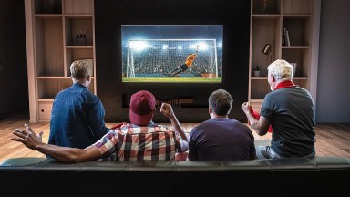 Empat pria duduk di sofa dan menikmati pertandingan sepak bola di TV